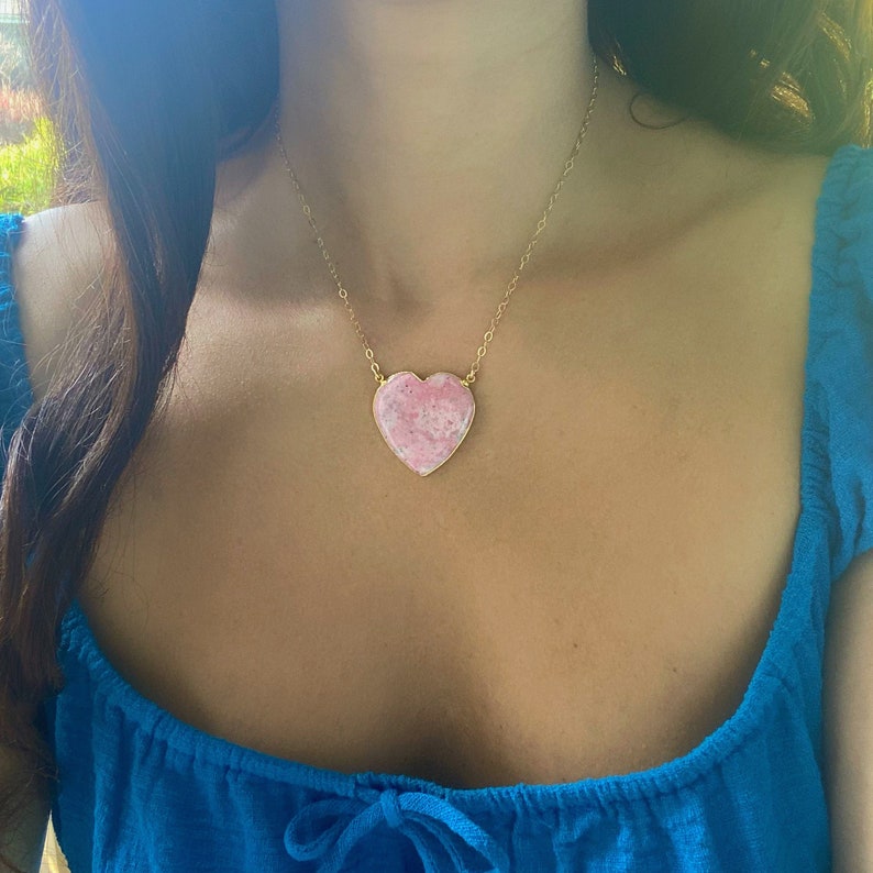 May include: A gold chain necklace with a large pink heart-shaped pendant. The pendant has a marbled pattern.
