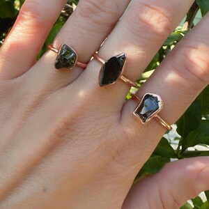 May include: Three rings with black gemstone settings on a rose gold band. The gemstones are different shapes and sizes.