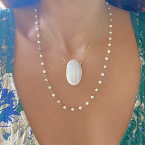May include: Two gold necklaces with white beads. The longer necklace has a large oval white stone pendant.