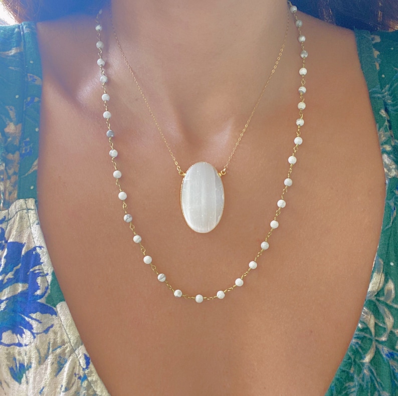 May include: Two gold necklaces with white beads. The longer necklace has a large oval white stone pendant.