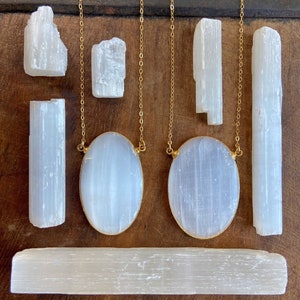 May include: Two gold chains with oval selenite pendants, and several selenite sticks of varying sizes. The selenite is a white, translucent crystal.