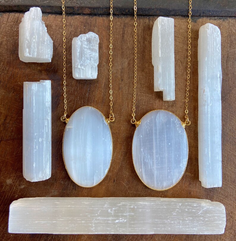 May include: Two gold chains with oval selenite pendants, and several selenite sticks of varying sizes. The selenite is a white, translucent crystal.