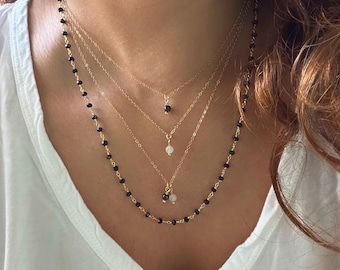 May include: A layered necklace with four chains. The top chain features black beads, the second chain has a small black pendant, the third chain has a small white pendant, and the bottom chain has a small black and white pendant.