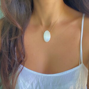 May include: A gold chain necklace with a large oval-shaped white gemstone pendant.