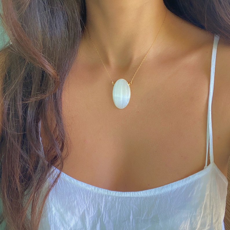 May include: A gold chain necklace with a large oval-shaped white gemstone pendant.