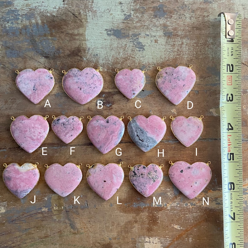 May include: Twelve pink heart-shaped stones with gold-toned jump rings. The stones have a marbled pattern and are arranged in four rows of three.