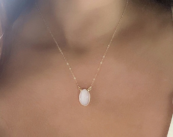 May include: A delicate gold chain necklace with a white oval gemstone pendant.