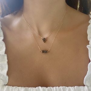 May include: Two gold necklaces with raw, irregular shaped, dark brown stones. The top necklace has a heart-shaped stone and the bottom necklace has a longer, rectangular stone.