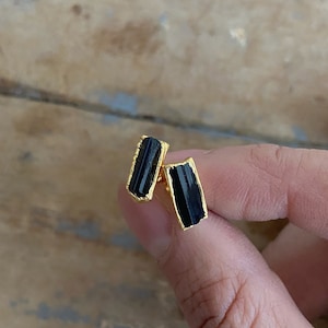 Puede incluir: Un par de pendientes de oro con piedras de turmalina negra. Las piedras son de forma rectangular y tienen un aspecto bruto y natural.