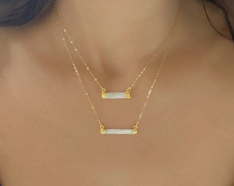 May include: Two gold necklaces with white bar pendants. The necklaces are layered, with the shorter necklace featuring a smaller bar pendant.