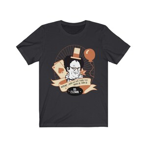 Könnte beinhalten: Dunkelgraues T-Shirt mit einer Cartoon-Illustration einer Person mit Zylinder und Brille, mit dem Text "Maybe I make my way thru this sorry ol world as clown." Enthält einen Ballon und Spielkarten.