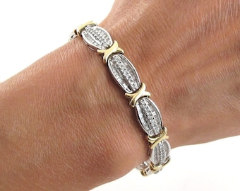 May include: A silver and gold bracelet with a row of oval-shaped links set with small diamonds. The bracelet is on a person's wrist.