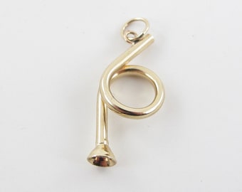 May include: A gold-colored metal charm in the shape of a French horn. The horn is curled and has a bell at the end.