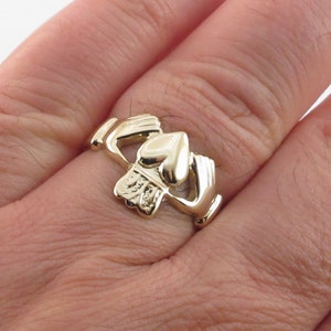 May include: A gold Celtic knot ring with a heart design. The ring is worn on a person's finger.