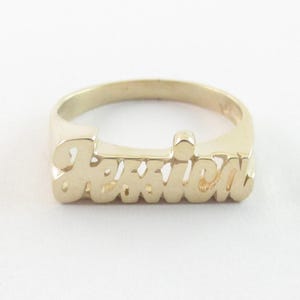 Könnte beinhalten: Goldfarbener Ring mit dem Namen "Jessica" in Schreibschrift. Der Ring hat ein Banddesign, wobei der Name das Hauptelement bildet. Der Hintergrund ist weiß.