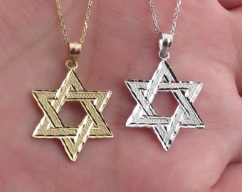 Puede incluir: Dos colgantes de Estrella de David en cadenas. Un colgante es de oro y el otro de plata. Ambos colgantes tienen un patrón de diamante.