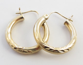 May include: A pair of gold-colored hoop earrings. One earring has a textured, diamond-like pattern on the lower half, while the other has a smooth finish. The earrings are displayed on a white background.