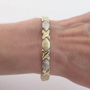 May include: A gold bracelet with a diamond-shaped pattern. The bracelet is made of two-toned gold, with a polished finish.