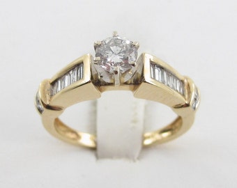 May include: A gold engagement ring with a round center diamond and smaller baguette diamonds on the band.