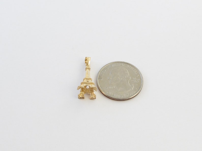 K&ouml;nnte beinhalten: Ein kleiner, goldfarbener Eiffelturm-Anh&auml;nger. Der Anh&auml;nger ist sehr detailliert, mit aufwendigen Gitterarbeiten und einer Schlaufe zum Befestigen. Eine M&uuml;nze liegt daneben zum Gr&ouml;&szlig;envergleich.