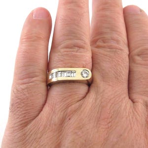 May include: A gold band ring with a single round diamond and a row of baguette diamonds.