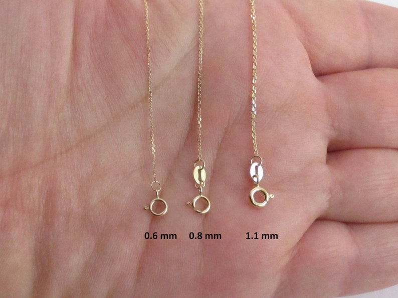 May include: Three gold chains of different thicknesses, 0.6 mm, 0.8 mm, and 1.1 mm, are shown on a hand. The chains are all the same length and are hanging straight down.