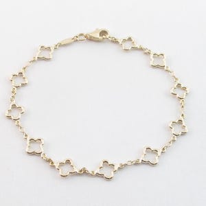 May include: A gold-colored bracelet featuring a delicate clover design. The bracelet is composed of multiple clover-shaped links connected by small chain segments, with a clasp closure. The jewelry is set against a white background.