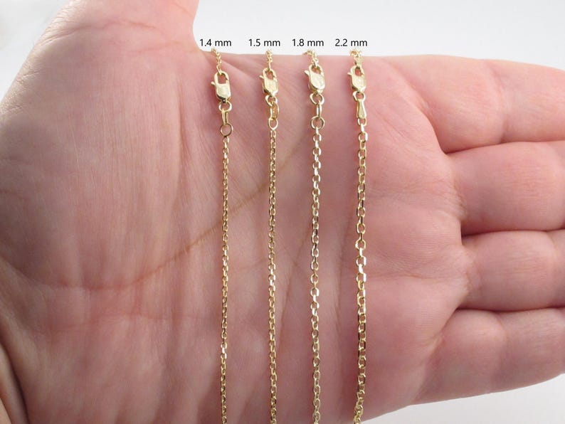 May include: Four gold-colored chain necklaces with lobster claw clasps are displayed. The chains vary in thickness, with labels indicating 1.4 mm, 1.5 mm, 1.8 mm, and 2.2 mm. The chains are shown against a light background.