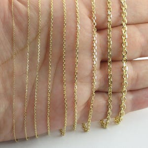 May include: A hand displays a variety of gold-colored chain necklaces. The chains vary in style and thickness, showcasing different link designs. The necklaces are presented against a neutral background, highlighting the jewelry's details.