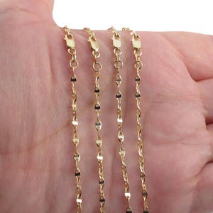 May include: Four delicate gold-colored necklaces with lobster claw clasps are displayed. The chains have a repeating pattern of small, flat, rectangular links. The necklaces are shown against a neutral background.