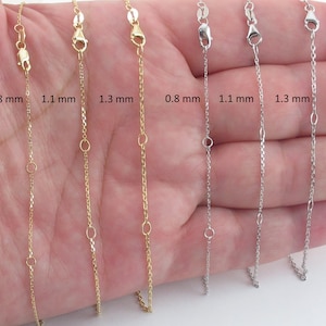 Könnte beinhalten: Fünf goldene und silberne Ketten in verschiedenen Stärken, auf einer Hand gezeigt. Die Ketten sind 0,8 mm, 1,1 mm und 1,3 mm dick.