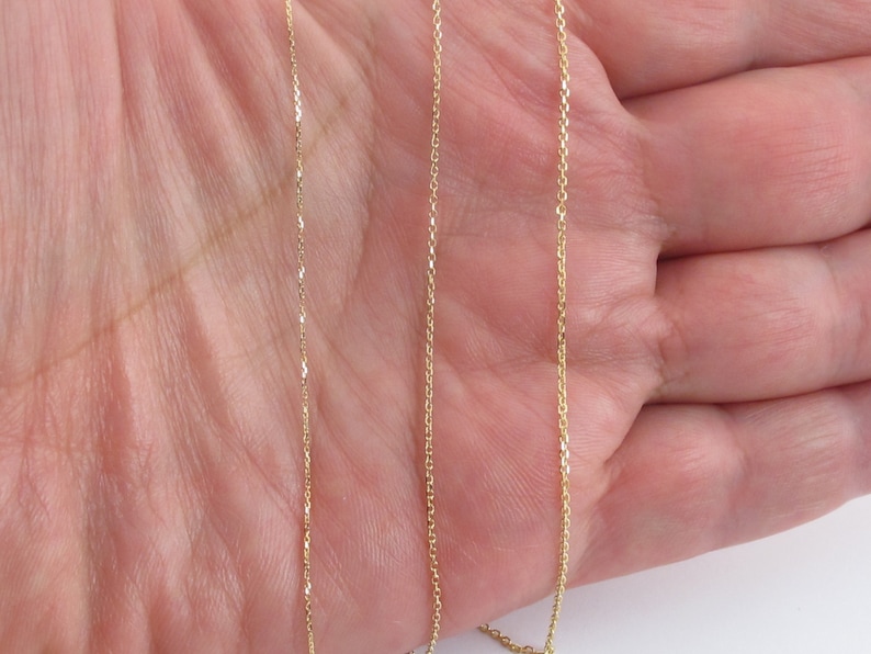 May include: Three gold chains of different lengths, displayed on a hand.