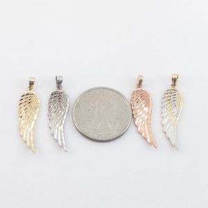 Op de afbeelding: Vier engelenvleugel hangers in goud, zilver en ros&eacute;goud. De hangers zijn ongeveer zo groot als een Amerikaanse kwart.