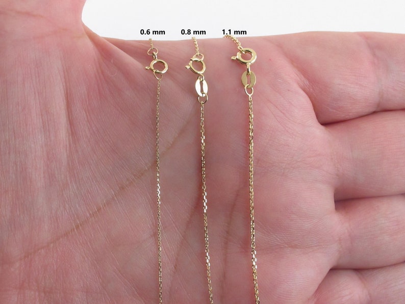 May include: Three gold chains of different thicknesses, 0.6 mm, 0.8 mm, and 1.1 mm, are displayed on a hand. The chains are all the same length and are made of a fine, delicate chain link.