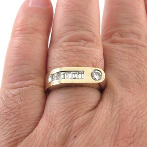 May include: A gold band ring with a row of baguette-cut diamonds and a single round diamond in the center.