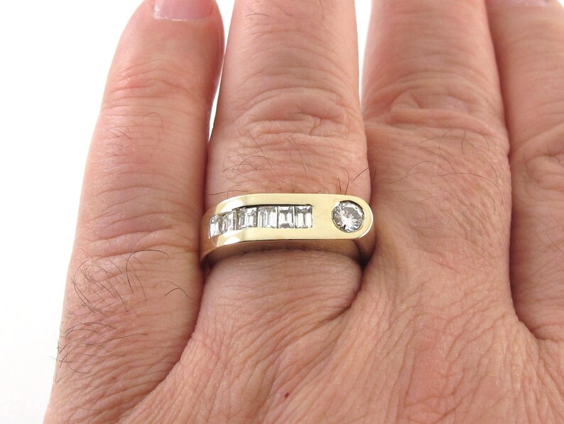 May include: A gold band ring with a row of baguette-cut diamonds and a single round diamond in the center.