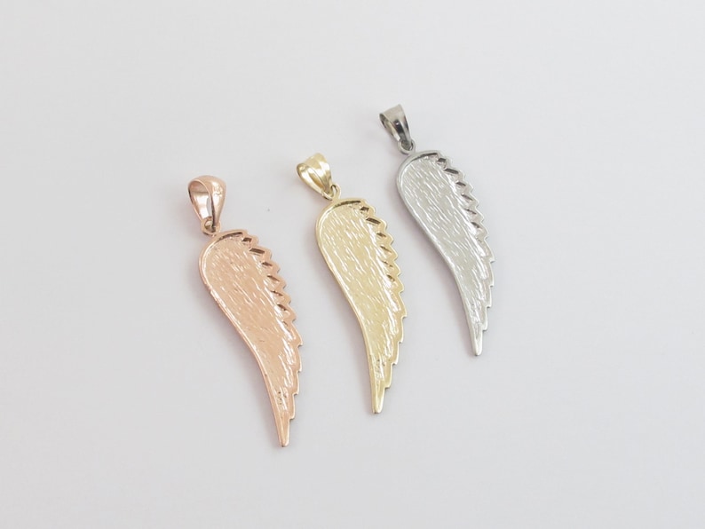 Op de afbeelding: Drie engelenvleugel hangers in verschillende metaal afwerkingen: goud, zilver en ros&eacute;goud. Elke hanger heeft een gedetailleerd vleugel ontwerp.