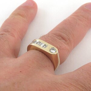 May include: A gold band ring with a single round diamond and a row of smaller diamonds set in the band.