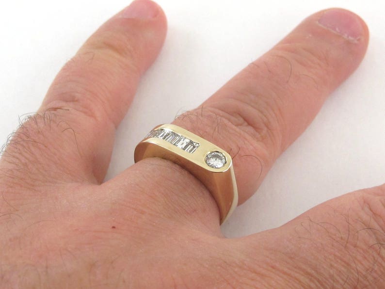 May include: A gold band ring with a single round diamond and a row of smaller diamonds set in the band.