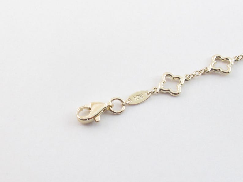 May include: Gold-toned bracelet with a clover design. The bracelet features a lobster clasp closure and a series of clover-shaped charms connected by small chain links. The background is plain white.
