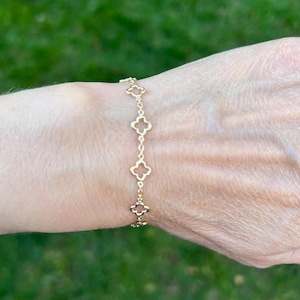 May include: Gold-colored bracelet featuring a series of four-leaf clover charms. The bracelet is delicate and appears to be made of a thin chain. The clover charms are evenly spaced along the chain, creating a simple yet elegant design.