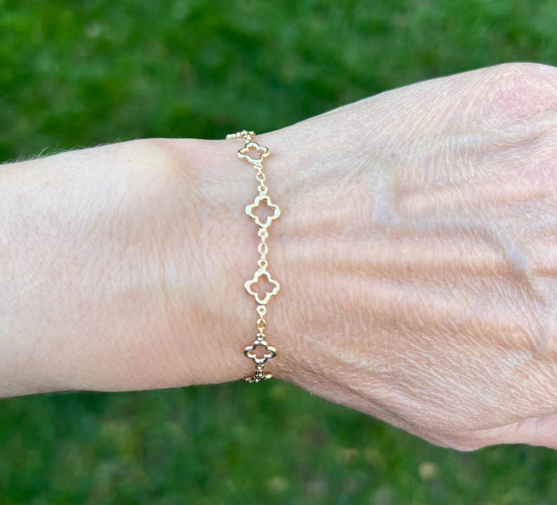 May include: Gold-colored bracelet featuring a series of four-leaf clover charms. The bracelet is delicate and appears to be made of a thin chain. The clover charms are evenly spaced along the chain, creating a simple yet elegant design.