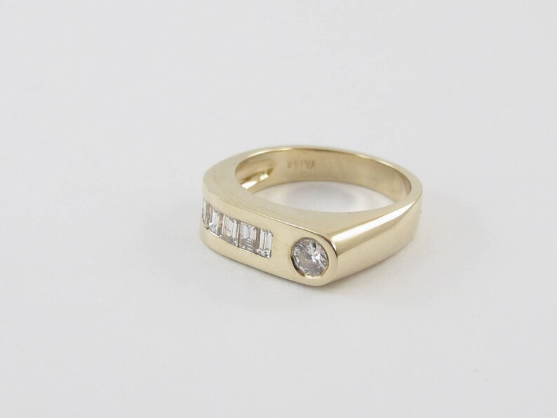 May include: A gold band ring with a single round diamond and a row of baguette diamonds.