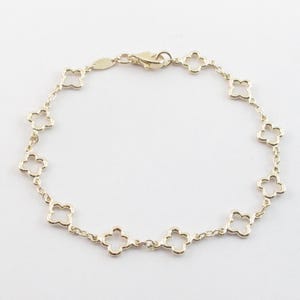 May include: A gold-colored bracelet featuring a delicate chain with clover-shaped links. The bracelet has a lobster clasp closure. The jewelry is displayed on a white background.