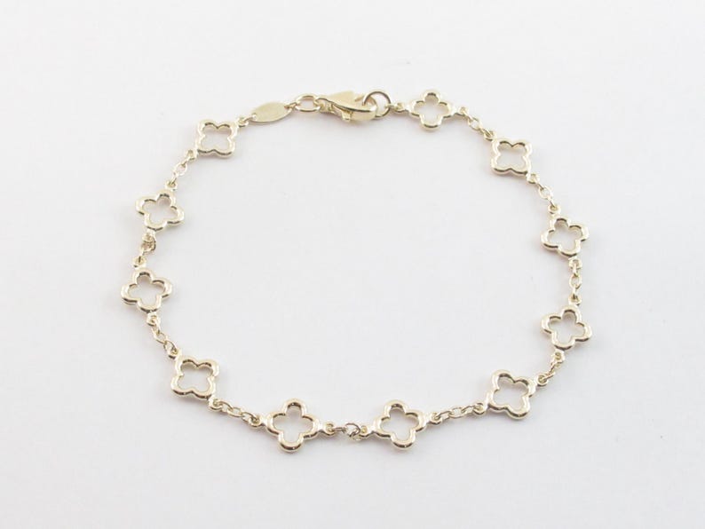 May include: A gold-colored bracelet featuring a delicate chain with clover-shaped links. The bracelet has a lobster clasp closure. The jewelry is displayed on a white background.
