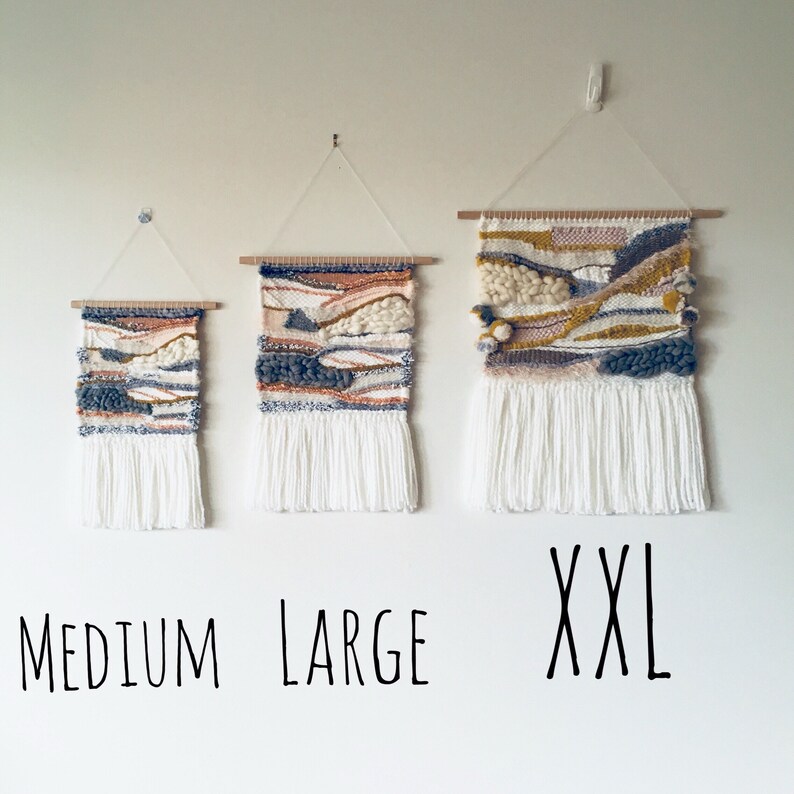 Three woven wall hangings in varying sizes; small, medium, and large.  The hangings feature a similar design with a color palette of off-white, beige, gray, and mustard yellow.  Each piece has a white fringe at the bottom. The sizes are labeled as 'MEDIUM', 'LARGE', and 'XXL' below the hangings.