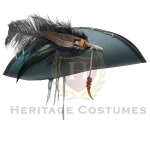 Puede incluir: Un sombrero de tres picos en color verde azulado oscuro con borde negro, adornado con una pluma negra grande, una pluma m&aacute;s peque&ntilde;a con patrones marrones y blancos, y un dije en forma de cuerno marr&oacute;n colgando de un cord&oacute;n. Se lee HERITAGE COSTUMES.