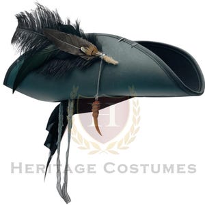Puede incluir: Un sombrero de tres picos de color verde oscuro con un grupo de plumas negras y marrones en el lateral. Una cadena plateada cuelga de la base de las plumas, conectada a un peque&ntilde;o dije curvo de color marr&oacute;n claro con forma de cuerno. Dos cintas de tela fina y deshilachada cuelgan.