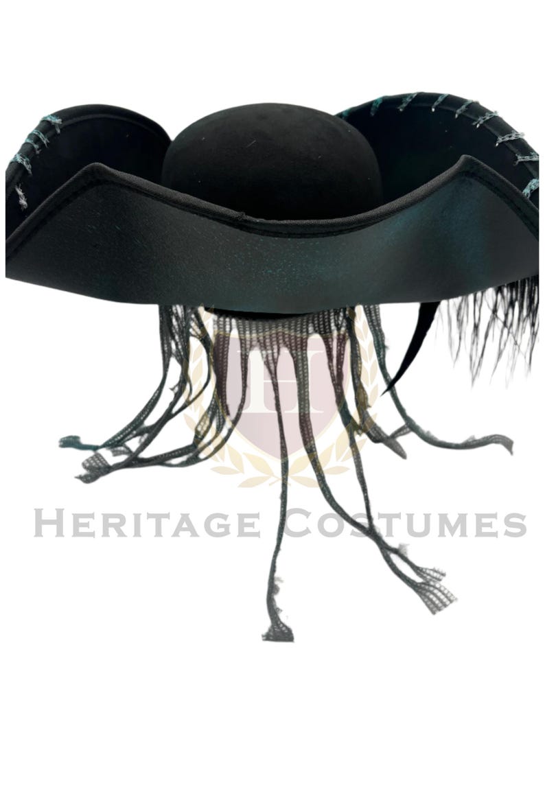 Puede incluir: Un sombrero de tres picos negro con un ala ancha y curva con costuras en color verde azulado a lo largo de los bordes. El sombrero est&aacute; adornado con tiras de tela negra largas y finas que cuelgan de la base de la copa y plumas negras.