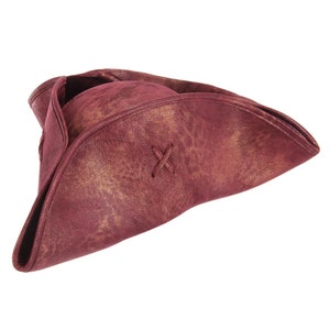 May include: A tricorn hat in a deep burgundy color with a distressed, mottled texture featuring gold-toned highlights. The hat has a wide, upturned brim on three sides and a small, decorative X-shaped stitch detail on the front section of the brim.